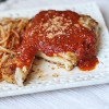 A photo of chicken parmesan on a white plate.