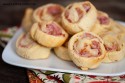 Bacon and cheese pinwheels stacked up on a square white plate.